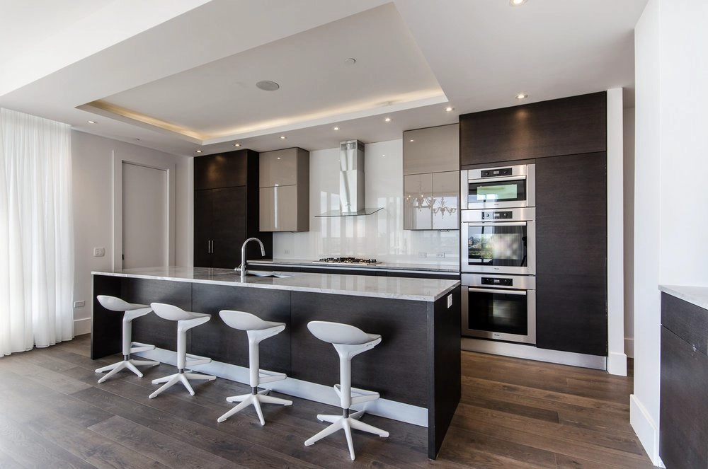 High-end cooktops & ovens installation with triple Miele ovens, chimney hood and built-in refrigerator in a modern Westmount kitchen.